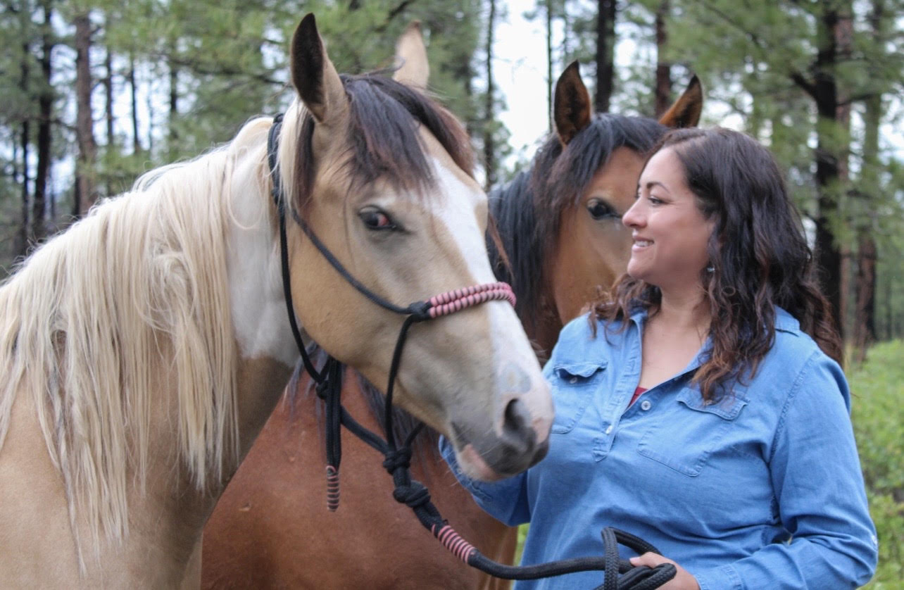 Vanessa Lucero with two horses in a forested New Mexico pasture
