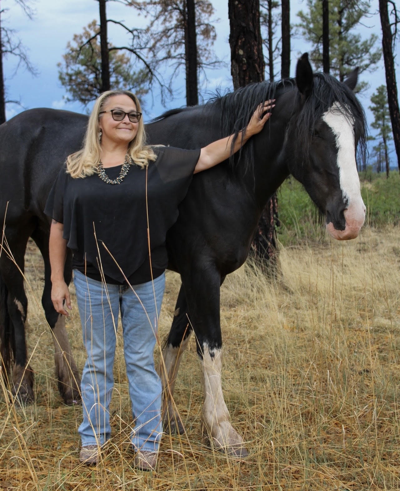 Curandero, a black and white paint horse, standing beside a participant in a New Mexico pasture