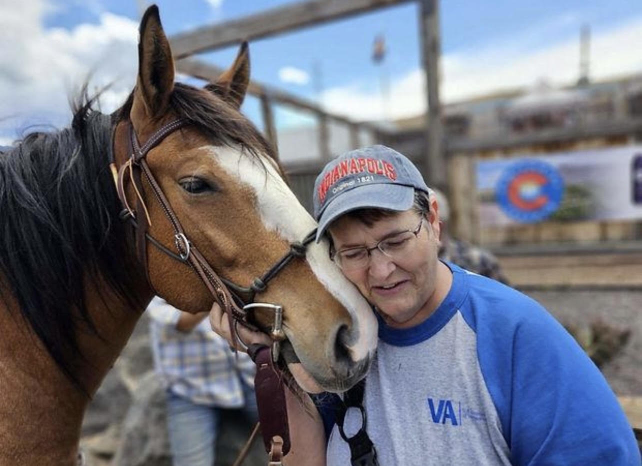 A veteran in a VA shirt sharing a quiet moment with a horse at Kinship Equine Therapy